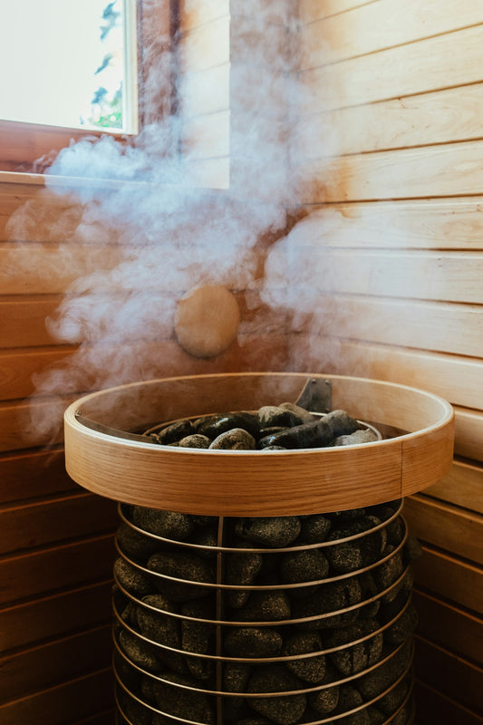 Steam rising from hot stones in a round sauna heater inside a wooden sauna