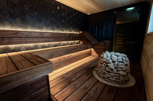 Modern wooden sauna with tiered benches, warm accent lighting and a stone-filled heater