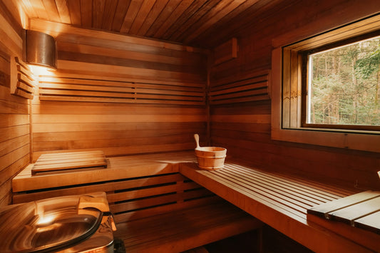 Empty wooden sauna with tiered benches, a wooden bucket and a window looking out to a forest