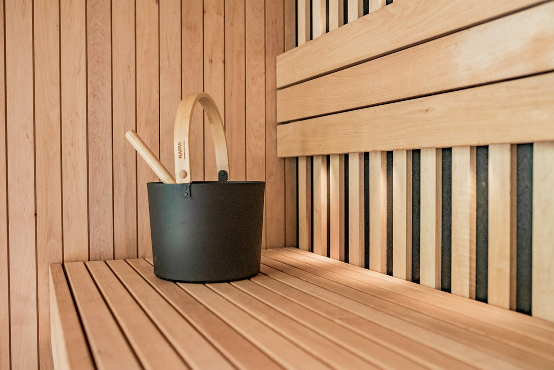 Wooden sauna bucket and ladle on a sauna bench next to a folded towel